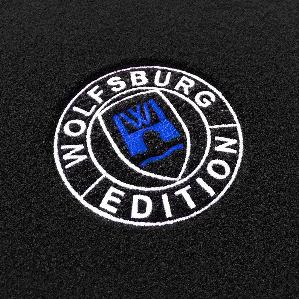 Das gestickte Wolfsburg Editions Logo auf einem schwarzen Teppich und das Logo ist in royalblau.